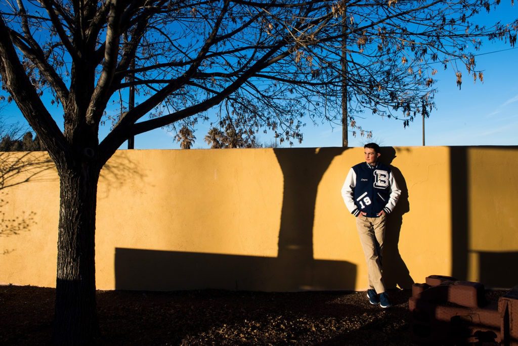 high-school-senior-boy-in-front-of-yellow-wall-at-sunset