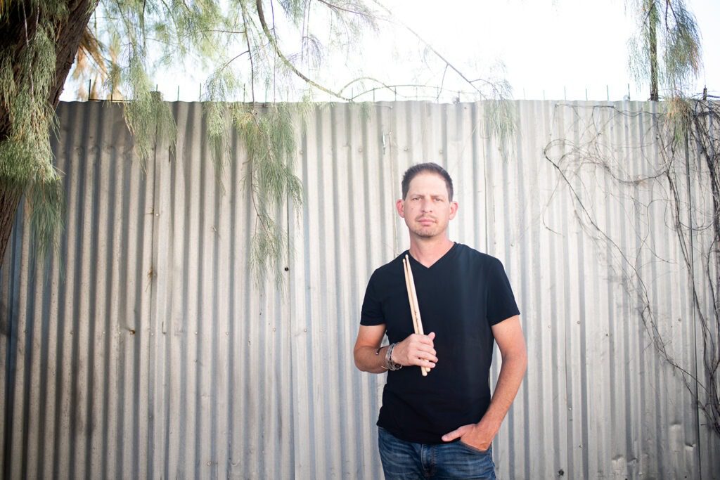 drummer-sitting-holding-drum-sticks-on-tin-wall