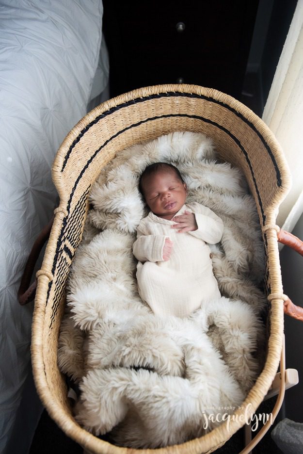 baby boy in a bassinet wearing a cream swaddle