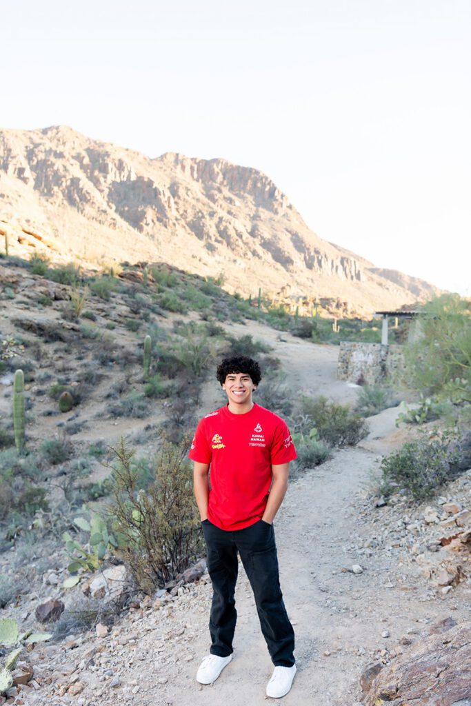 High school senior guy standing on desert trail in Tucson Arizona smiling during sunrise senior photo session at Gates Pas