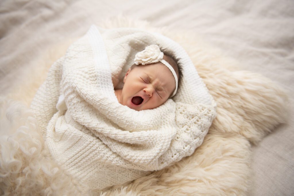 yawning newborn baby girl in cream knitted blanket 